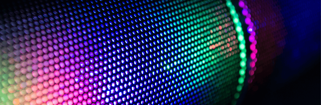 Image upclose of a round tubular speaker with bands of green and purple lighting up the hexagon shapes on the tube